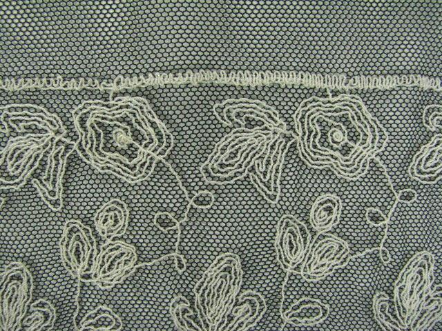 Claudia showing in closeup the ivory color version of a Leafy rayon Floral roses design Embroidered on a black nylon Mesh