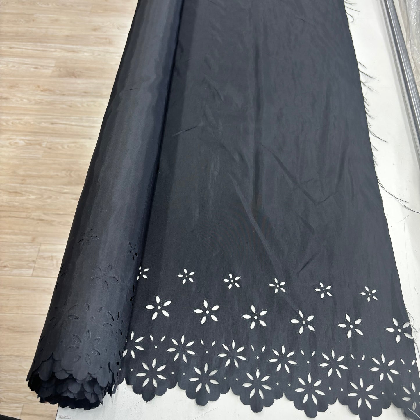 Showing the Blowout Black fabric with white floral cut-out details on a wooden floor